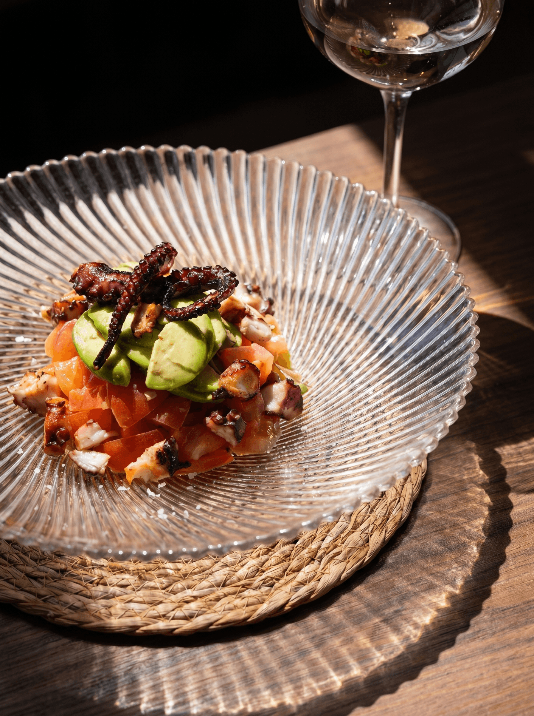 Grilled octopus salad with tomato and avocado, on a glass plate · Acontramar, La Herradura