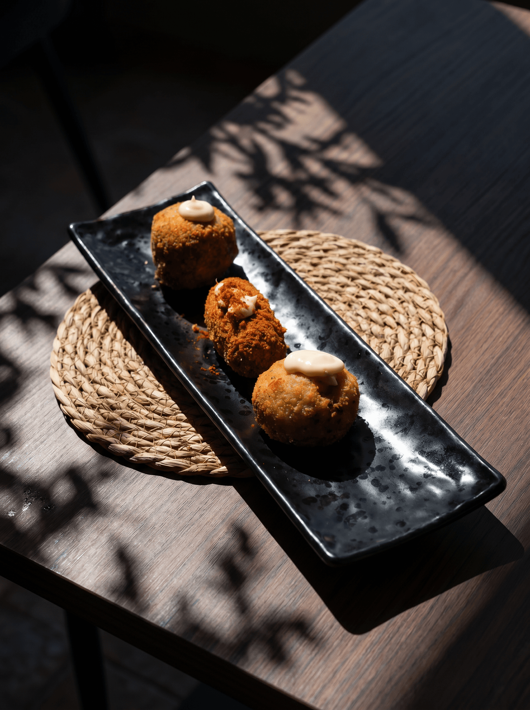 Three freshly fried croquettes on a long black plate · Acontramar, La Herradura