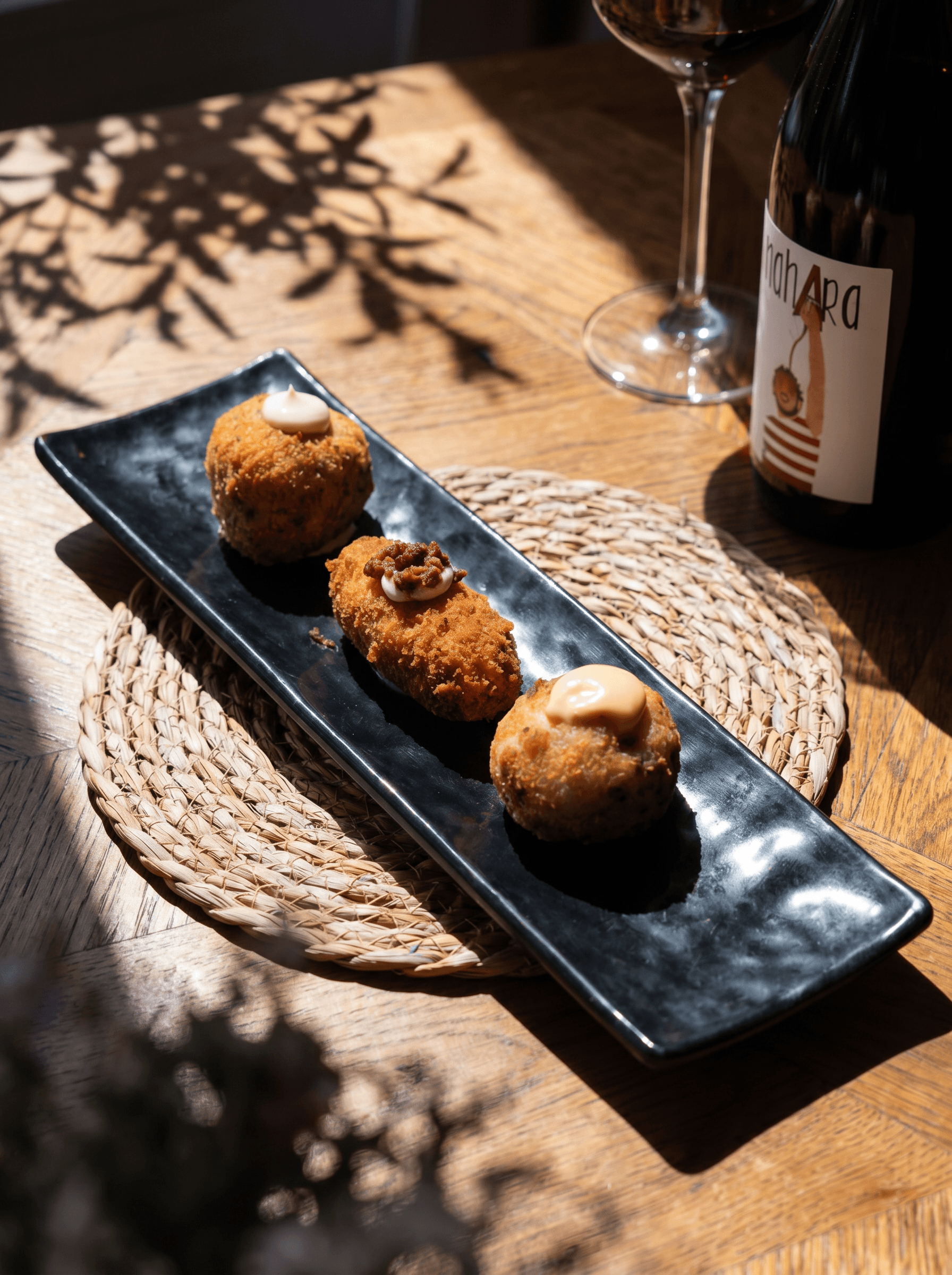 Our trilogy of croquettes on a long plate, beside a glass of red wine · Acontramar, La Herradura